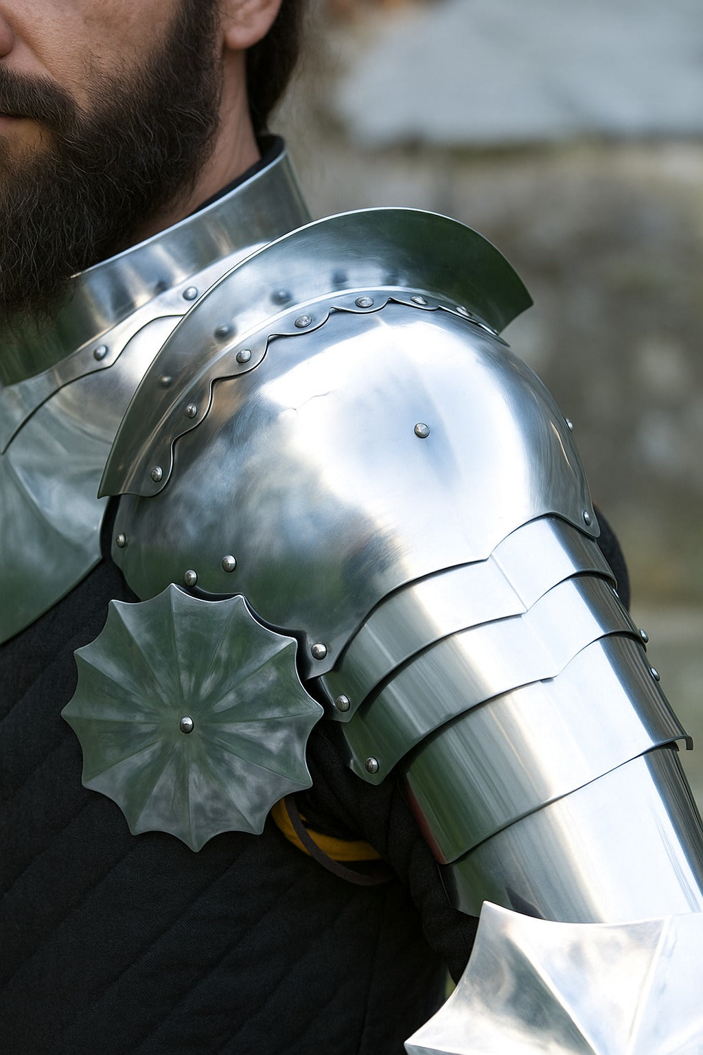 Medieval knight wearing handcrafted polished steel armor suit with detailed shoulder and arm guards
