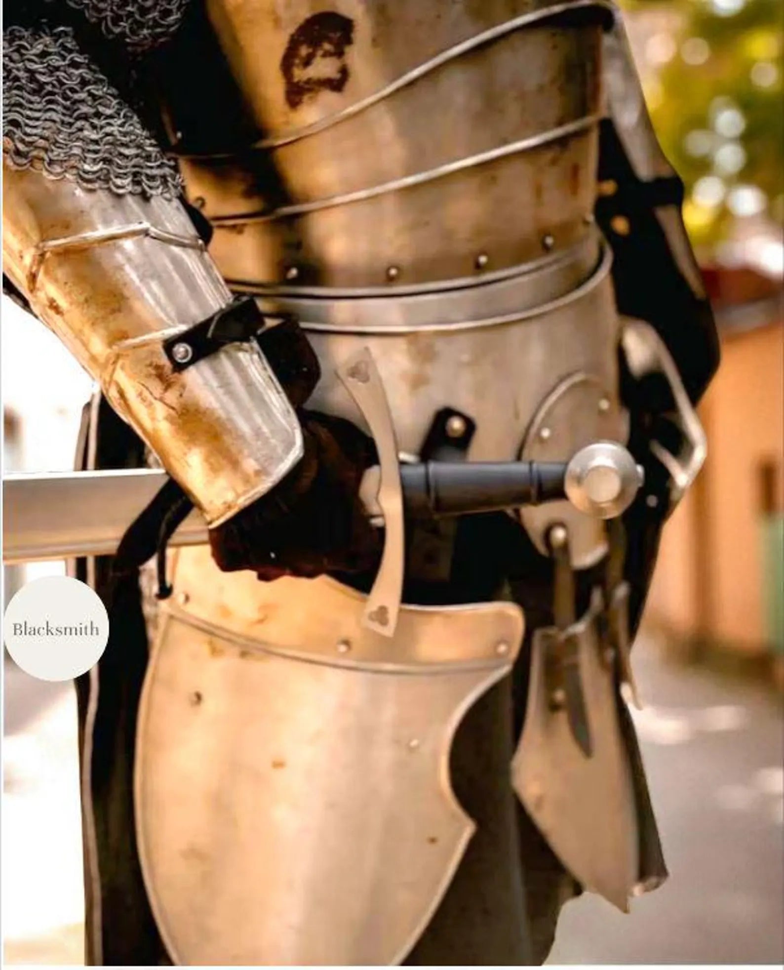 Person wearing a full medieval steel knight armor suit with helmet, holding a sword.