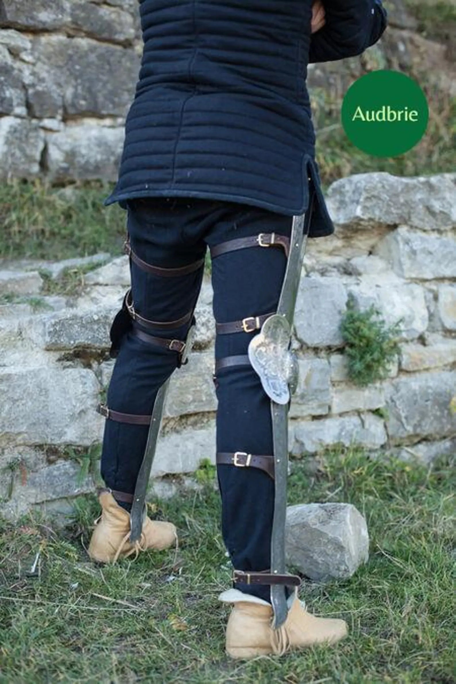 Person wearing navy riding pants with leather straps against a stone wall background