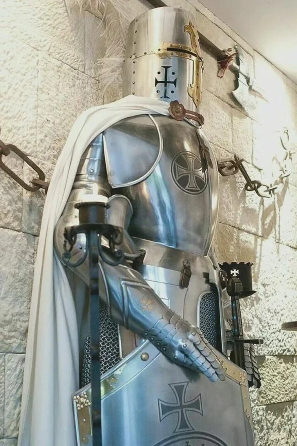 Knight in full armor with a white cape against a stone wall background